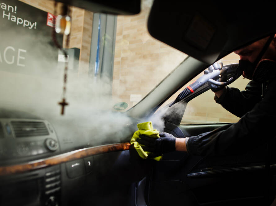 A close-up of a car's air vents being cleaned with a steam cleaner, demonstrating the removal of dust and allergens.