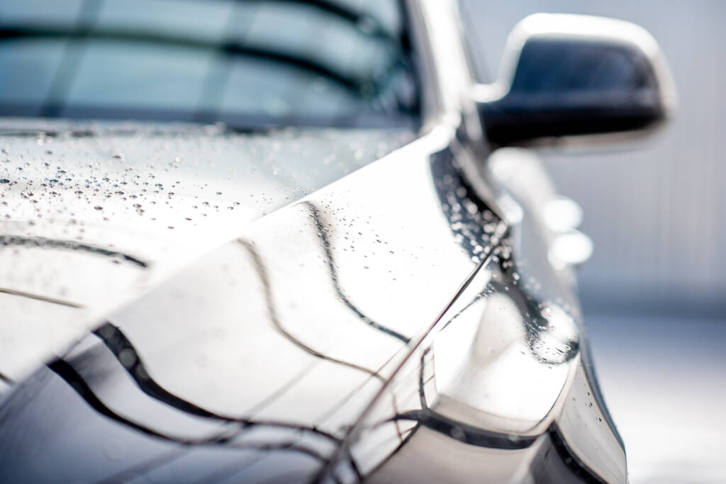 A professional detailer applying car wax to a black car, achieving a deep, reflective shine.