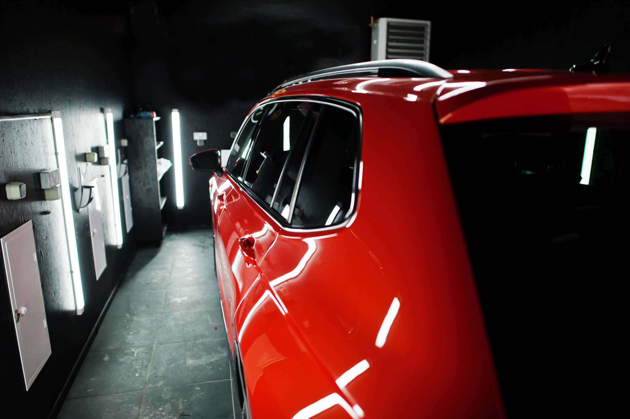 A hand applying a coat of wax to a red car's hood, creating a deep, reflective shine.