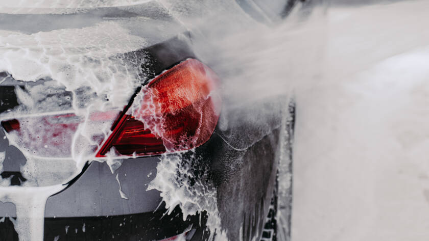 A hand applying car wax to a car's hood, resulting in a mirror-like finish.