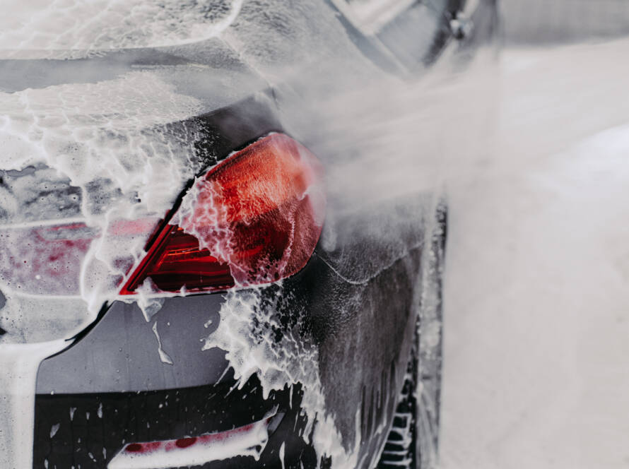 A hand applying car wax to a car's hood, resulting in a mirror-like finish.