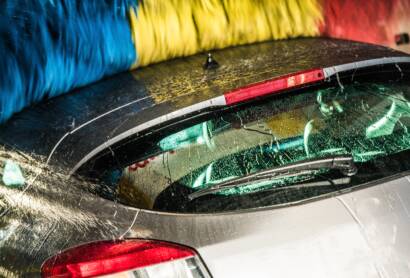 A close-up photo of a hand applying car wax to a red car, emphasizing the glossy finish.