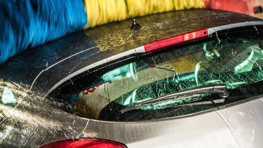 A close-up photo of a hand applying car wax to a red car, emphasizing the glossy finish.