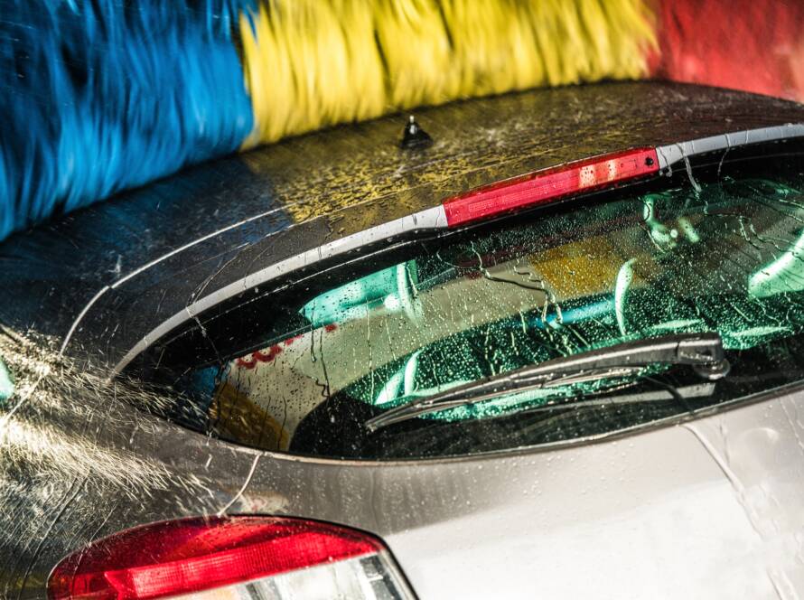 A close-up photo of a hand applying car wax to a red car, emphasizing the glossy finish.