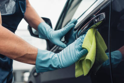 A hand applying car wax to a black car, showcasing a deep, reflective shine.