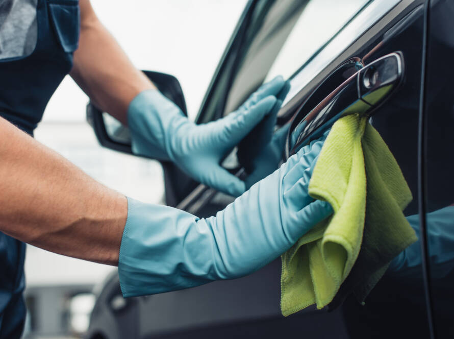 A hand applying car wax to a black car, showcasing a deep, reflective shine.