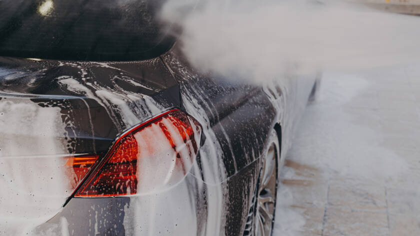 A smiling 85AutoSpa detailer carefully hand-washing a car.