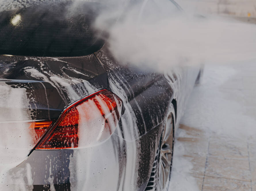 A smiling 85AutoSpa detailer carefully hand-washing a car.