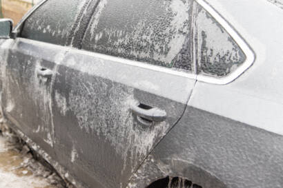 A hand applying car wax to a black car, showcasing a deep, reflective shine.