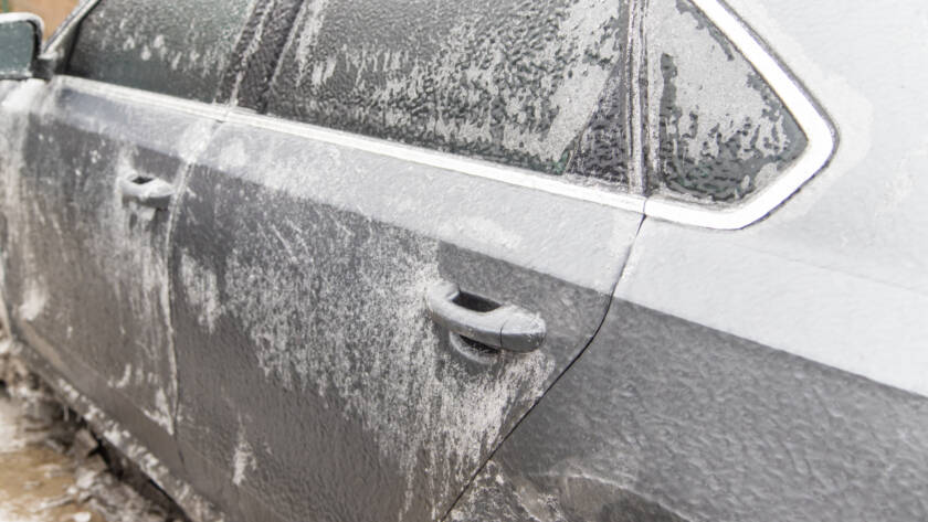 A hand applying car wax to a black car, showcasing a deep, reflective shine.