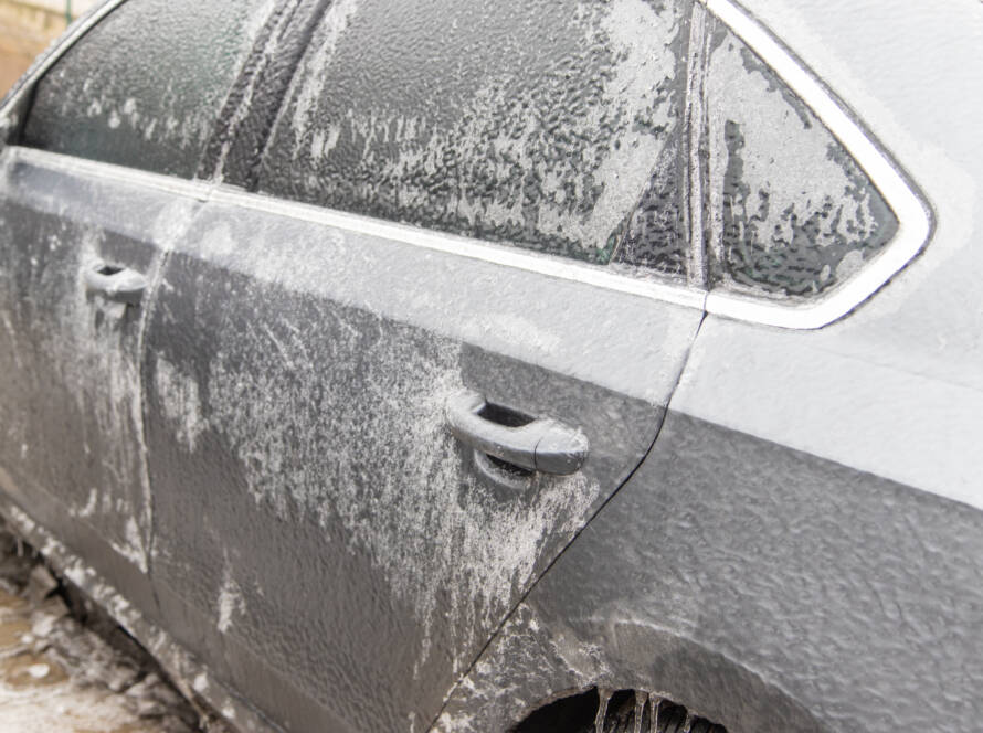 A hand applying car wax to a black car, showcasing a deep, reflective shine.